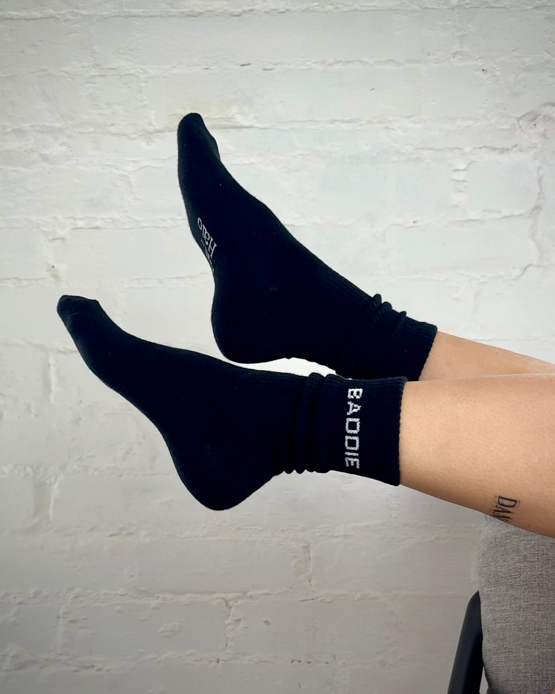 Black socks with 'BAODE' branding worn by a person against a light gray brick wall.