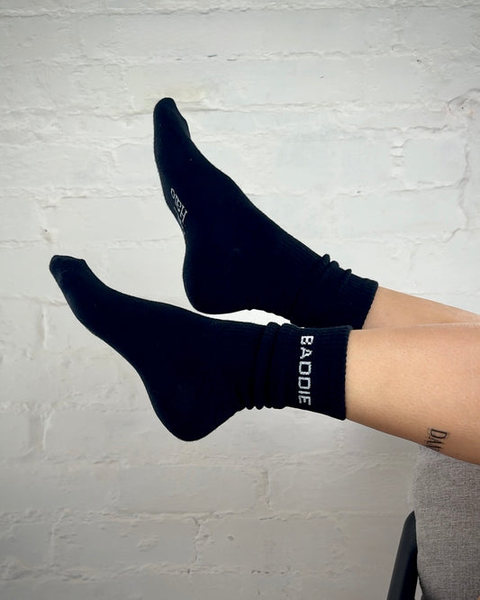Black socks with 'BAODE' branding worn by a person against a light gray brick wall.