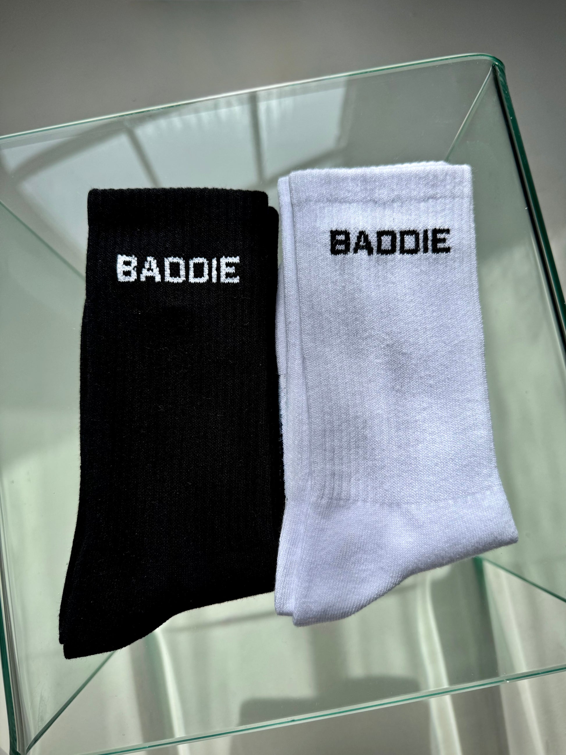 Black and white socks with 'BADDIE' text on a glass surface